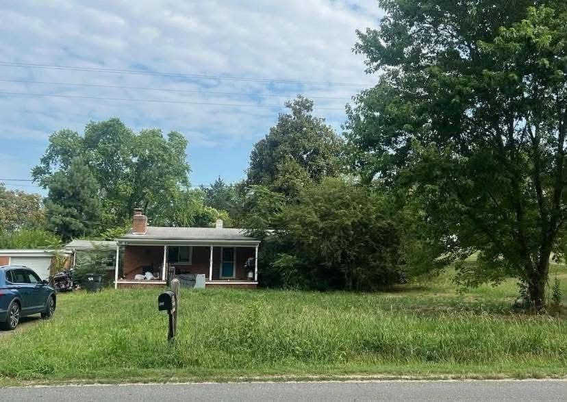 The brick ranch before, mostly hidden by tall grass and bushes